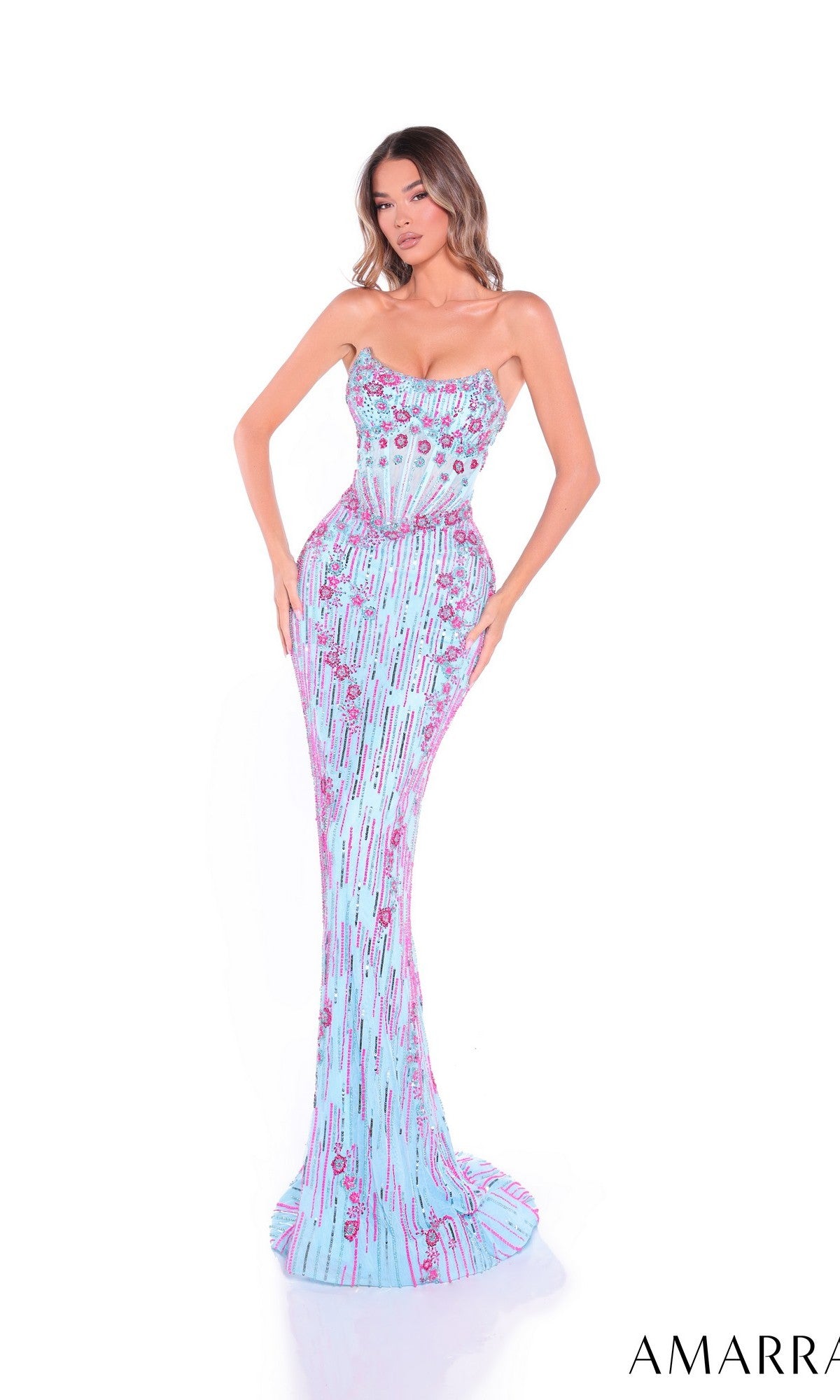 A woman stands against a white background wearing the Amarra 89057, a strapless, form-fitting blue prom dress with pink sequin detailing and a floor-length design.